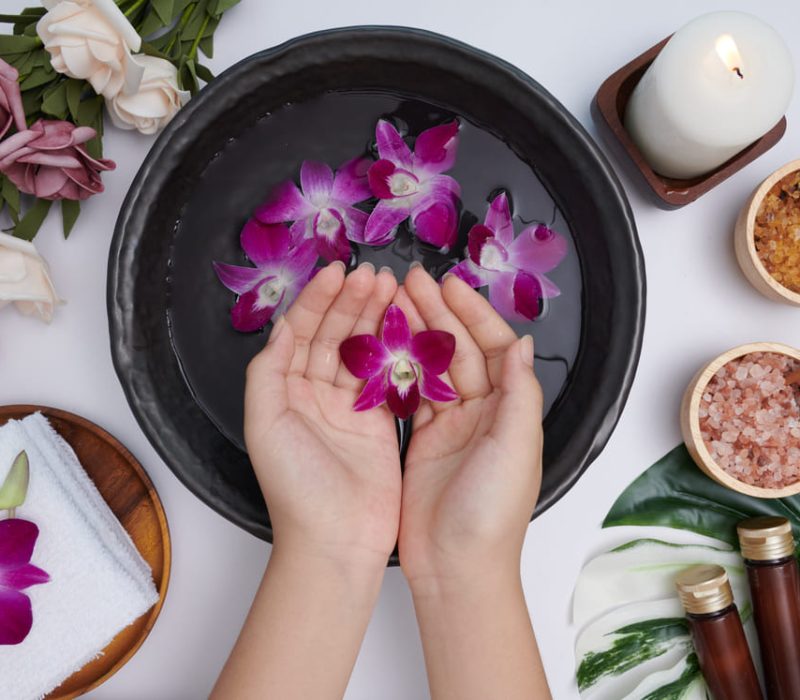 woman-soaking-her-hands-bowl-water-flowers-spa-treatment-product-female-feet-hand-spa-massage-pebble-perfumed-flowers-water-candles-relaxation-flat-lay-top-view (1) (1)
